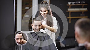 A pretty stylist by the hair makes a hairstyle for the lucky visitor of the salon, a woman cuts her hair with a trimmer