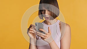Pretty surprised girl chatting with friends in social network look amazed  on yellow background. Wow face