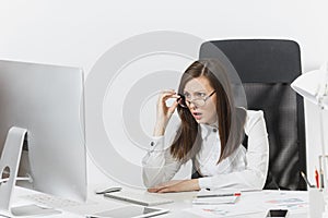 Beautiful business woman in suit and glasses working at computer with documents in light office