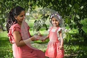 A pretty swarthy woman is walking with her daughter in park at bird cherry tree