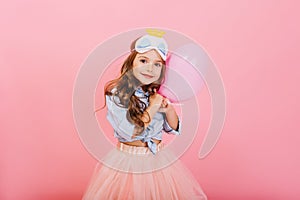 Pretty sweet little girl with long brunette hair hugging balloon, looking to camera isolated on pink background