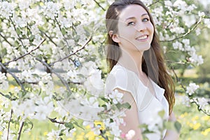 Pretty sweet tender young girl with a bright smile with long blond hair among the blossoming apple trees