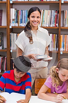 Pretty teacher helping pupils in library