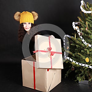 Pretty teen girl opening gift by Christmas tree