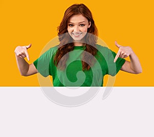 Pretty Teen Girl Pointing Fingers At Blank Poster, Yellow Background