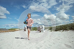 Pretty teen girl running with ball on white sand of beautiful beach with dunes at Baltic sea