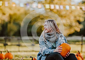 Pretty teen girl sitting on a pumpkin`s field holding a pumpkin and smile