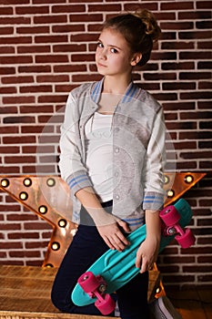 Pretty teen girl with skateboard over brick wall