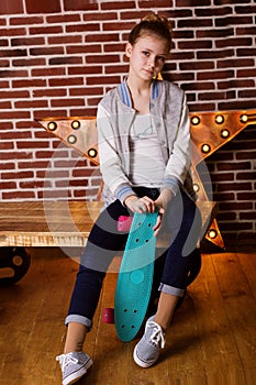 Pretty teen girl with skateboard sitting in studio