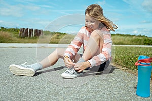 Pretty teen girl smiling and sitting on ground tie shoelaces at summer day