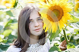 Pretty teen girl standing in a field near beautiful sunflower. The girl is genuinely smiling