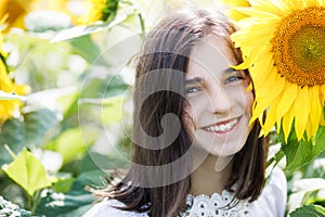 Pretty teen girl standing in a field near beautiful sunflower. The girl is genuinely smiling
