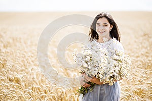 Pretty teen girl standing in a field among wheat. Girl holding a large bouquet of flowers in her hands