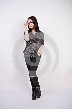 Pretty teen girl wearing fashion casual shirt and black torn jeans posing with eyeglasses on white studio background