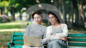 Pretty teenage daughter typing on laptop with mother in park