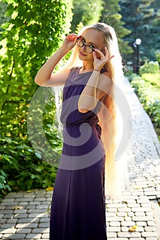 Pretty teenage girl 14-16 year old with curly long blonde hair in beautiful adult dress in the green park in a summer day outdoors