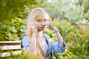 Pretty teenage girl 14-16 year old with curly long blonde hair and in glasses in the green park in a summer day outdoors.