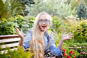 Pretty teenage girl 14-16 year old with curly long blonde hair and in glasses in the green park in a summer day outdoors.