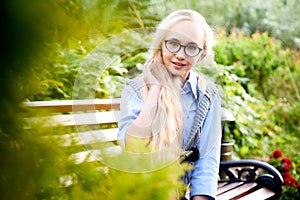 Pretty teenage girl 14-16 year old with curly long blonde hair and in glasses in the green park in a summer day outdoors.