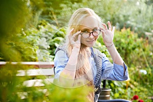 Pretty teenage girl 14-16 year old with curly long blonde hair and in glasses in the green park in a summer day outdoors.