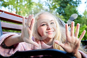 Pretty teenage girl 14-16 year old with curly long blonde hair in the green park on the bench in a summer day outdoors