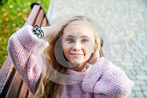 Pretty teenage girl 14-16 year old with curly long blonde hair in the green park on the bench in a summer day outdoors. Beautiful