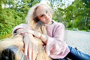 Pretty teenage girl 14-16 year old with curly long blonde hair in the green park on the bench in a summer day outdoors. Beautiful