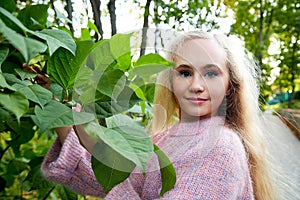 Pretty teenage girl 14-16 year old with curly long blonde hair in the green park in a summer day outdoors. Beautiful portrait