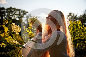 Pretty teenage girl 14-16 year old with curly long blonde hair in the green park with white flower in a summer day outdoors and