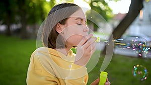 Pretty teenage girl blowing soap bubbles on a sunset. Child having fun in a park in summer.