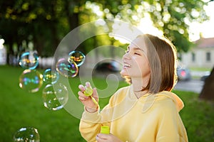 Pretty teenage girl blowing soap bubbles on a sunset. Child having fun in a park in summer