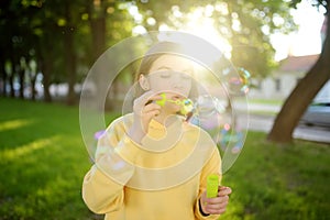 Pretty teenage girl blowing soap bubbles on a sunset. Child having fun in a park in summer
