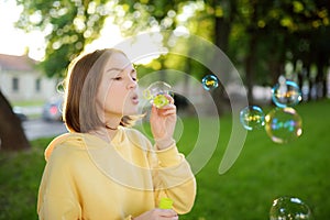 Pretty teenage girl blowing soap bubbles on a sunset. Child having fun in a park in summer