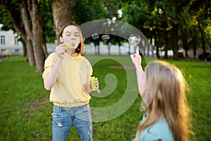 Pretty teenage girl blowing soap bubbles on a sunset. Children having fun in a park in summer