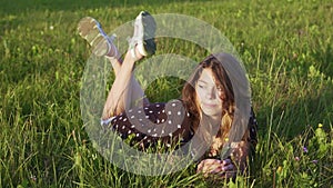 pretty teenage girl in a dress is lying on the green grass