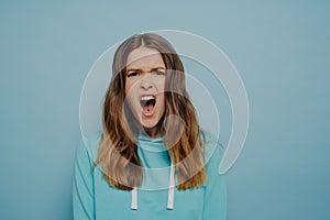 Pretty teenage girl expressing angry disbelief posing isolated over blue background