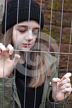 Pretty teenage girl gripping a wire fence