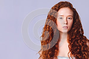 Pretty teenage girl with long curly red hair on a lilac background in the studio