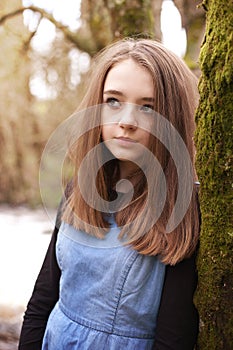 Pretty teenage girl looking upwards whilst leaning against a tree