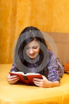 Pretty teenage girl lying in bed and reading a book