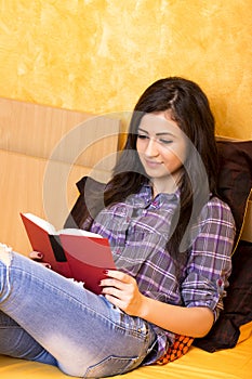 Pretty teenage girl lying in bed and reading a book