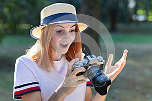 Pretty teenage girl with red hair looking amazed in photo camera in summer park