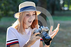 Pretty teenage girl with red hair looking amazed in photo camera in summer park