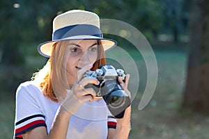 Pretty teenage girl with red hair looking amazed in photo camera in summer park