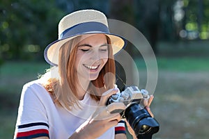 Pretty teenage girl with red hair taking picture with photo camera in summer park