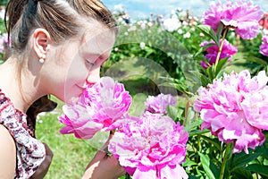 Pretty teenage girl smelling pink blossoming peony flowers in pa