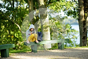 Pretty teenage girl using a smart phone sitting on a bench. Cute young girl having fun during forest hike on beautiful summer day