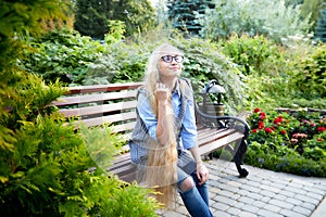 Pretty teenage girl 14-16 year old with curly long blonde hair and in glasses in the green park in a summer day outdoors.