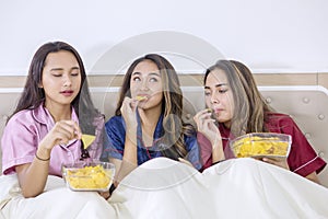Pretty teenage girls enjoying chips in bed
