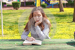 Pretty teenager girl reading a book and studying homework at the summer park